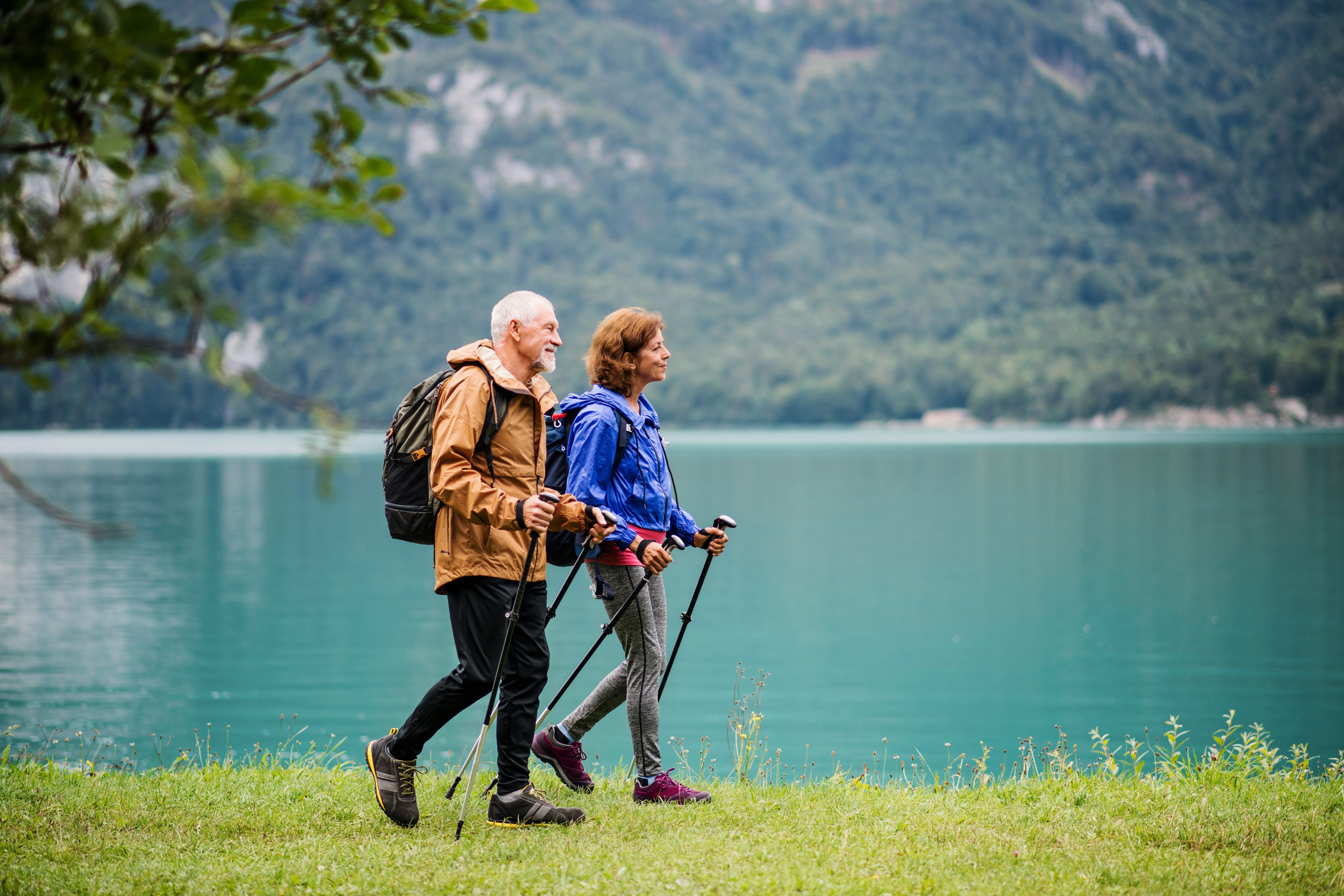 A side view of senior pensioner couple hiking by lake in nature.